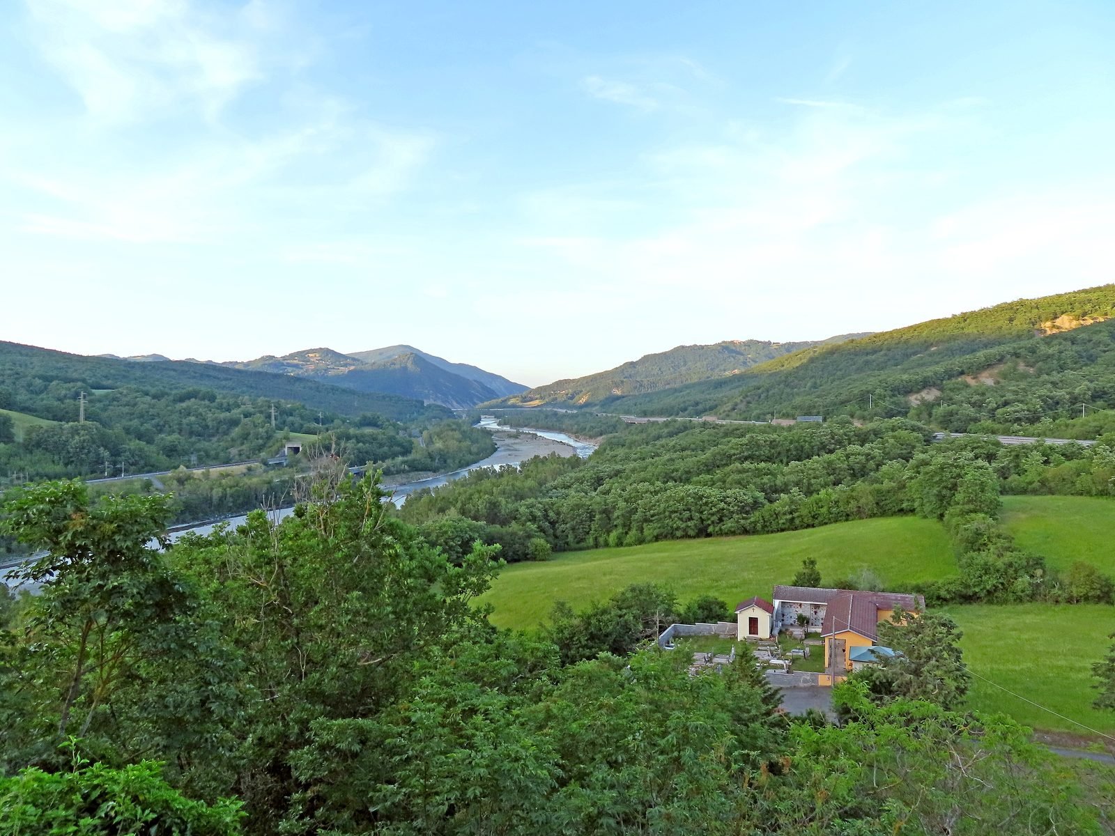 Vista panorâmica de um vale estreito entre serras arborizadas, com o rio Taro correndo ao fundo.