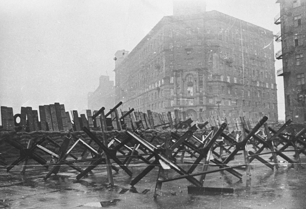 Fileiras de ouriços antitanque de trilhos cruzados e uma barricada de madeira atravessam uma rua de Moscou diante de um prédio alto