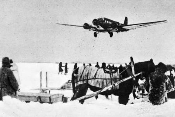 Avião de transporte trimotor baixando sobre um campo nevado, com um cavalo atrelado a um trenó e soldados em primeiro plano